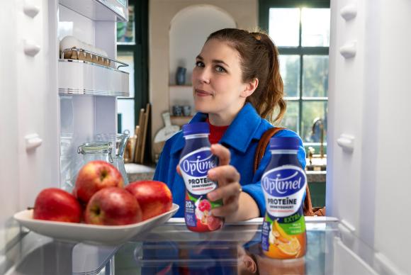 Vrouw pakt flesje Optimel Proteïne Extra uit de koelkast.